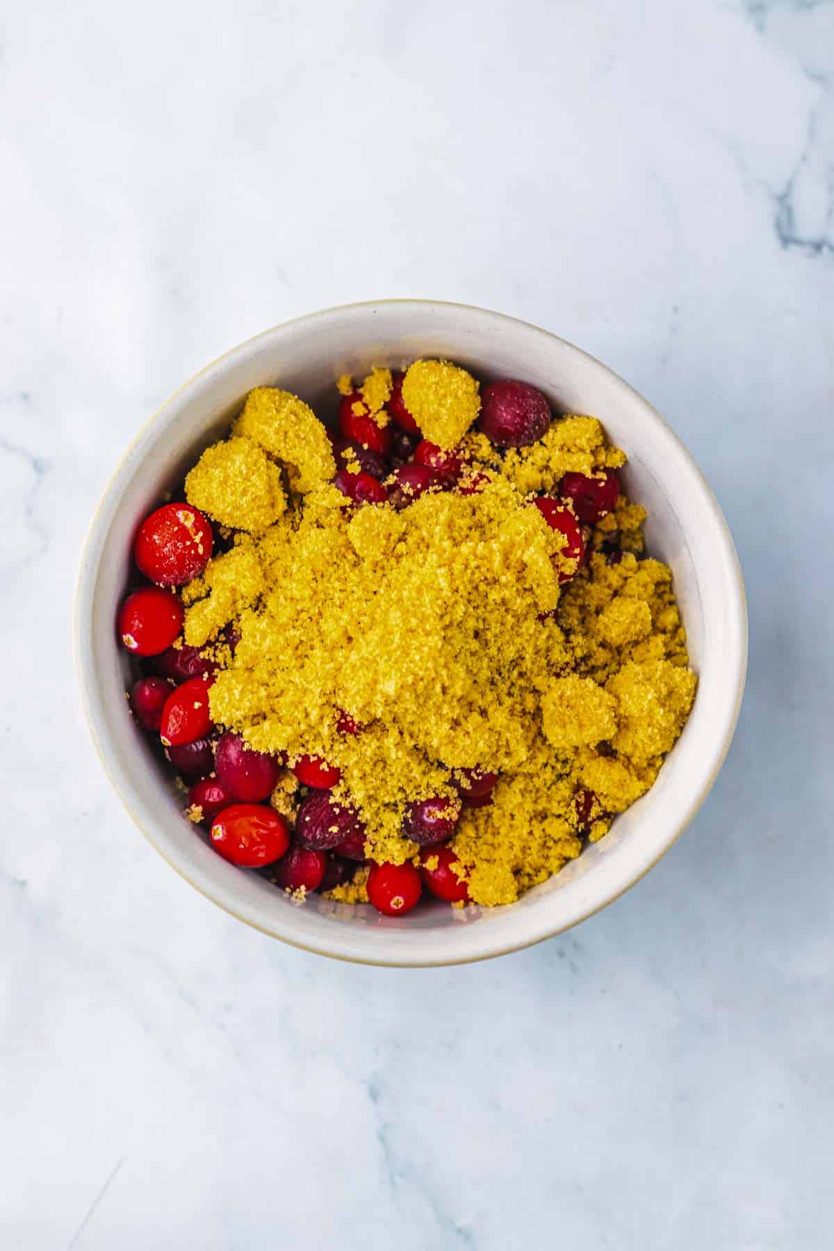 A bowl of fresh cranberries topped with a pile of brown sugar on a marble surface, perfect for creating a sweet glaze for Roasted Cranberry Chicken.