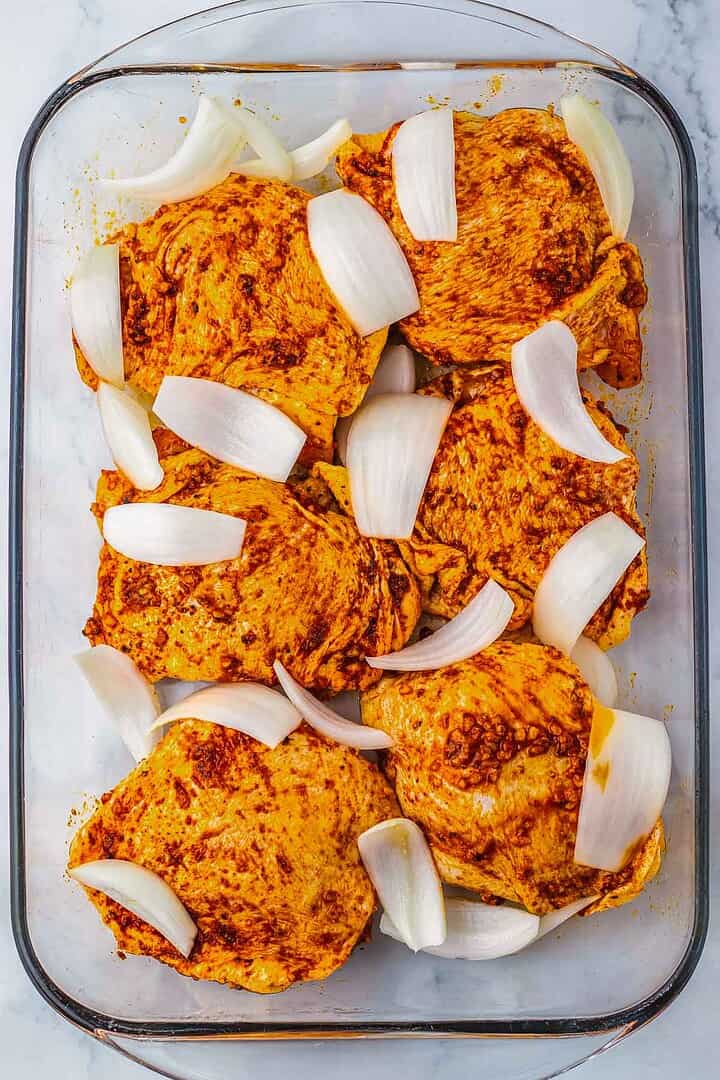 Raw seasoned chicken thighs and chopped onions arranged in a glass baking dish, ready to be cooked for delicious Roasted Cranberry Chicken Thighs.
