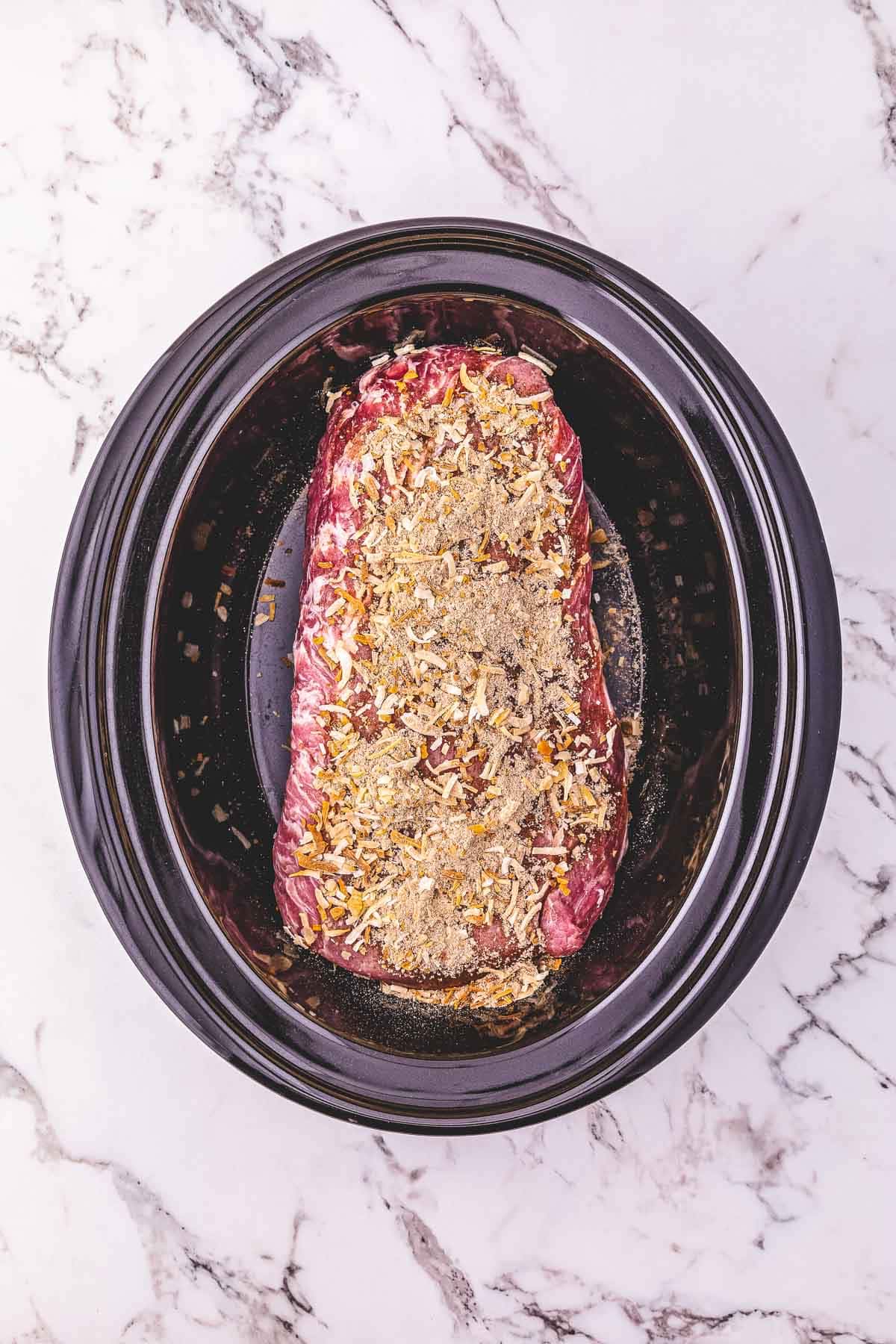 Raw seasoned pork loin in a Crockpot on a white marble countertop, ready to be cooked.