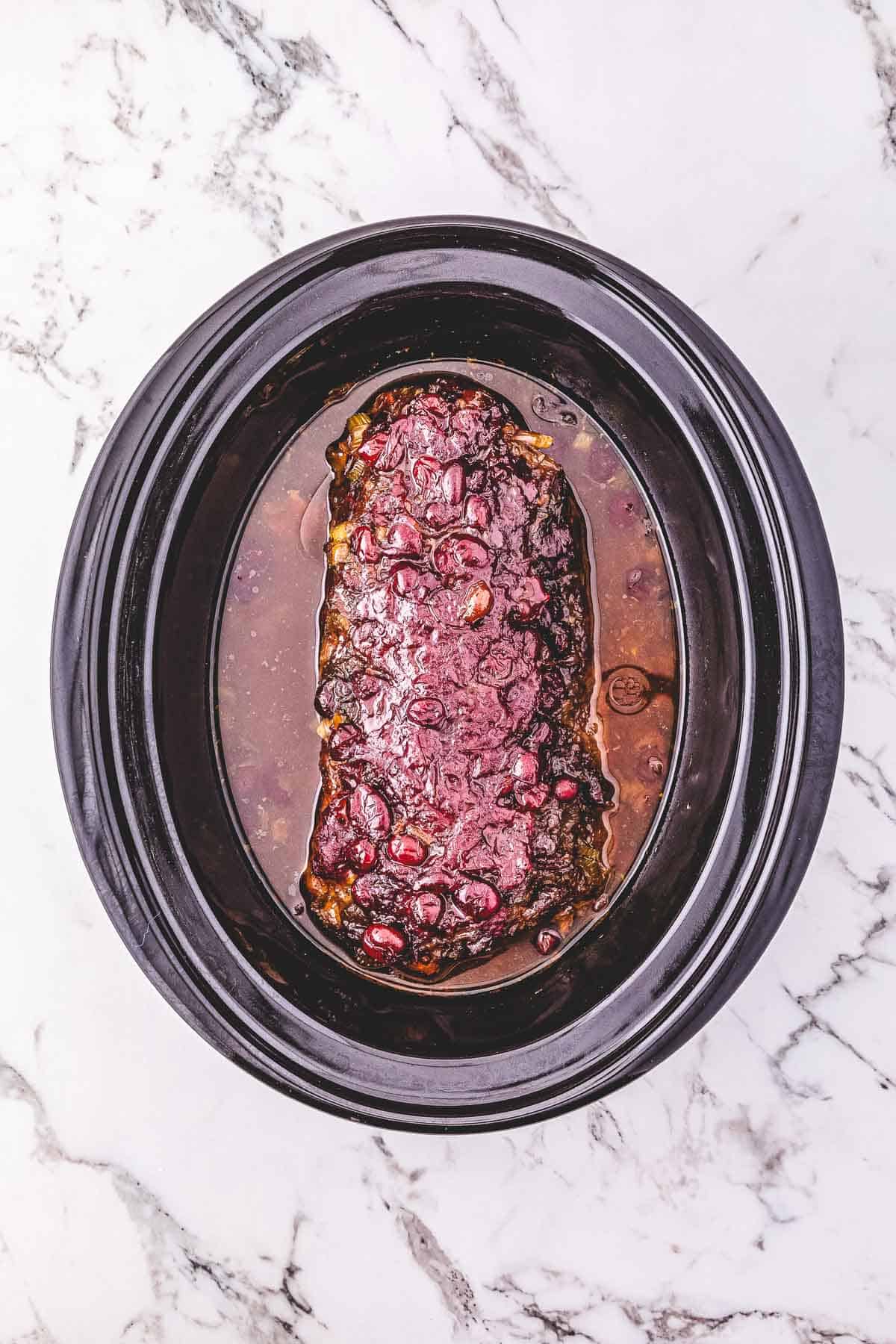 Cranberry-covered pork loin meatloaf cooked in a Crockpot sits on a marble countertop.