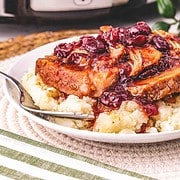 Pork loin chops with cranberry sauce served over mashed potatoes, with a Crockpot in the background.