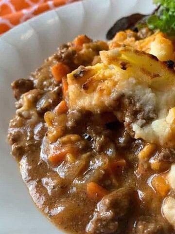 A plate of shepherd's pie with ground meat, vegetables, mashed potatoes, and a side of green salad.