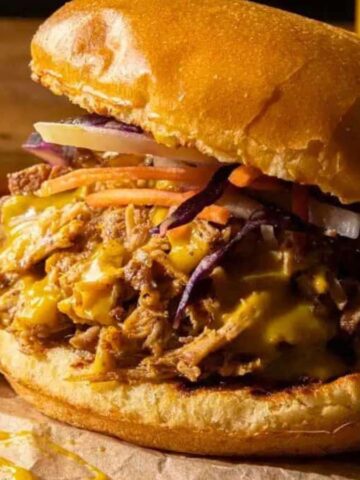 Pulled pork sandwich with melted cheese and slaw on a toasted bun, served on brown paper.