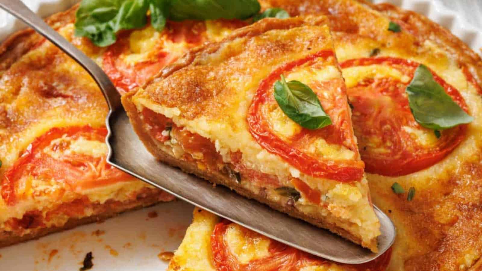 A slice of tomato pie on a white plate with a serving utensil, and a whole tomato pie in a white fluted dish, are shown on a marble surface with a small bowl of spices and basil leaves.