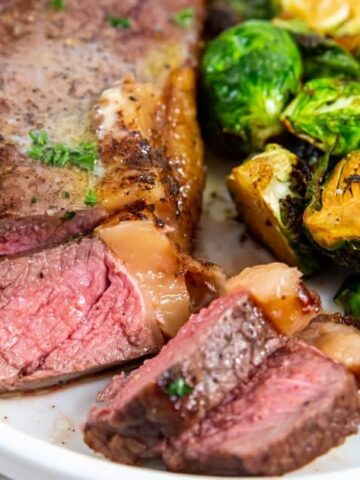 A plate with sliced medium-rare steak and roasted Brussels sprouts, served with a fork.