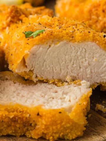 Sliced crispy breaded chicken breast on a wooden board, garnished with a small green herb.
