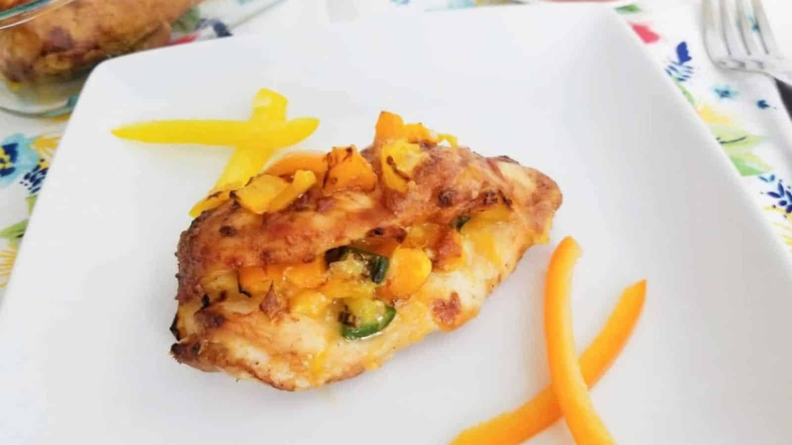 Stuffed chicken breast with melted cheese and vegetables, garnished with yellow pepper strips on a white plate.