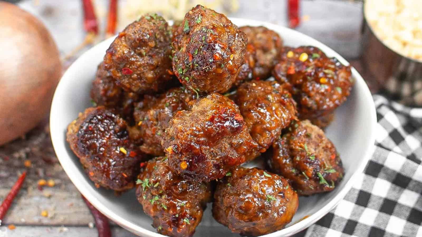 Golden meatballs with a sprinkle of herbs on a white plate, with marinara sauce.
