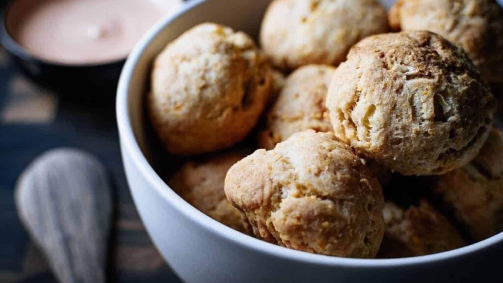 A white bowl filled with golden-brown biscuits, with a dipping sauce in the background.