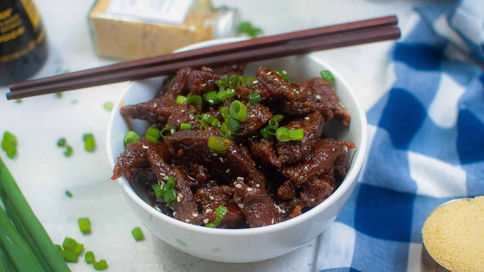 Closeup of crispy beef in a bowl with green onions and sesame seeds.
