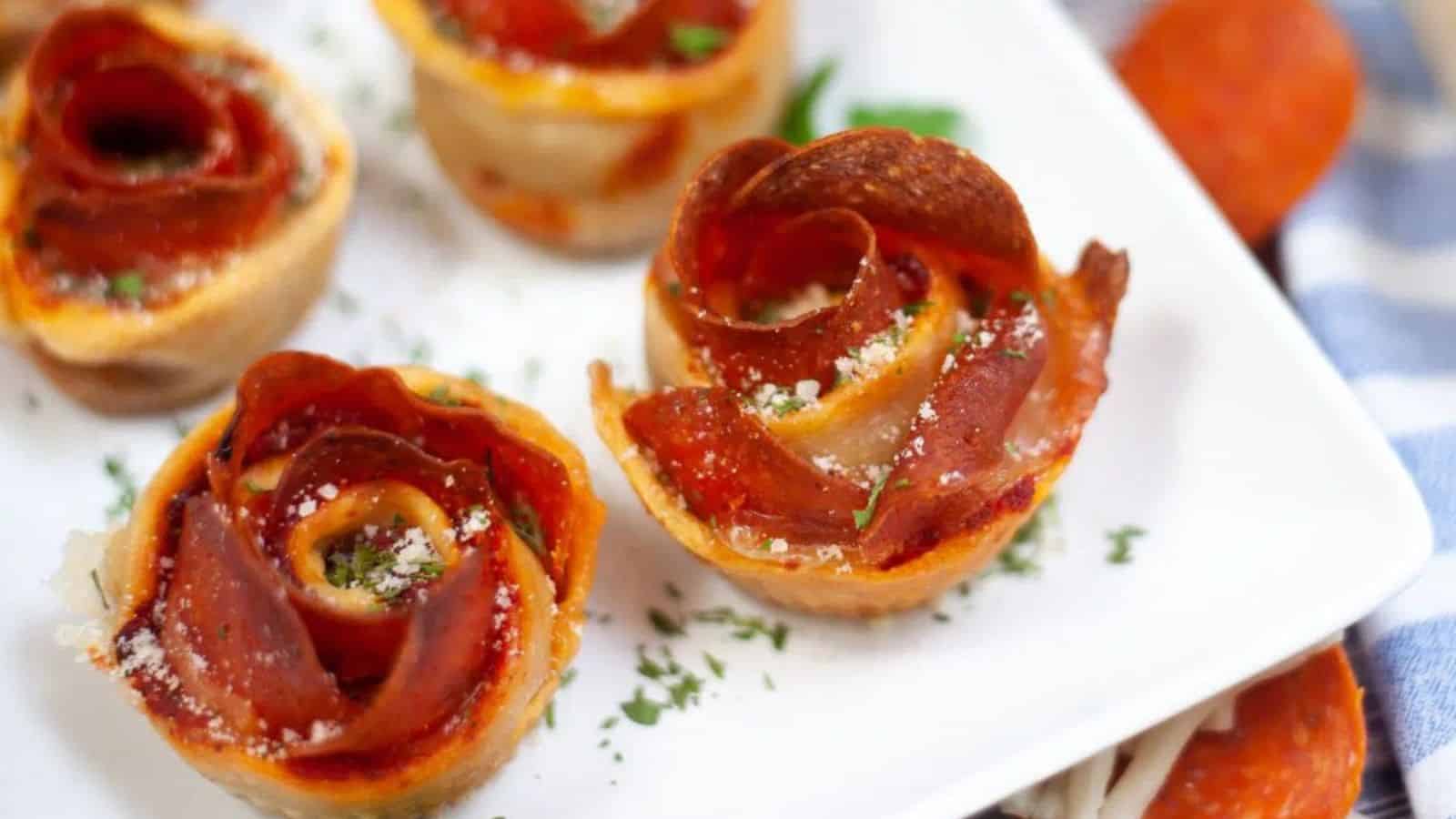Rose-shaped pepperoni and cheese pastry appetizers on a white plate, garnished with parsley and grated cheese.