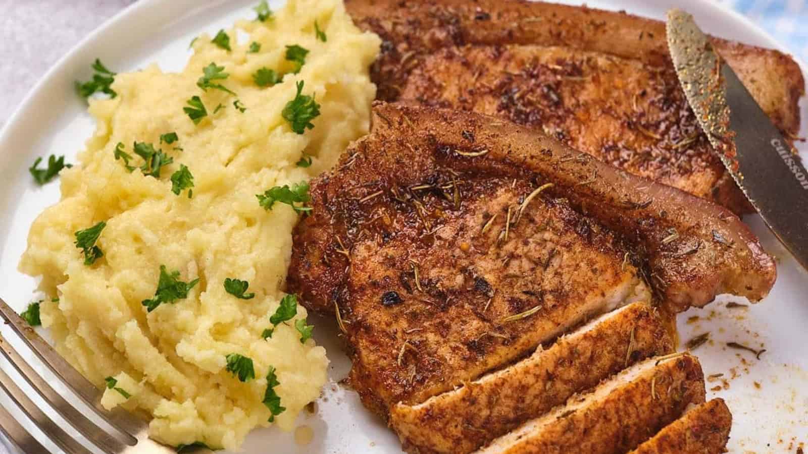 A serving of seasoned pork chops with a side of mashed potatoes on a white plate.