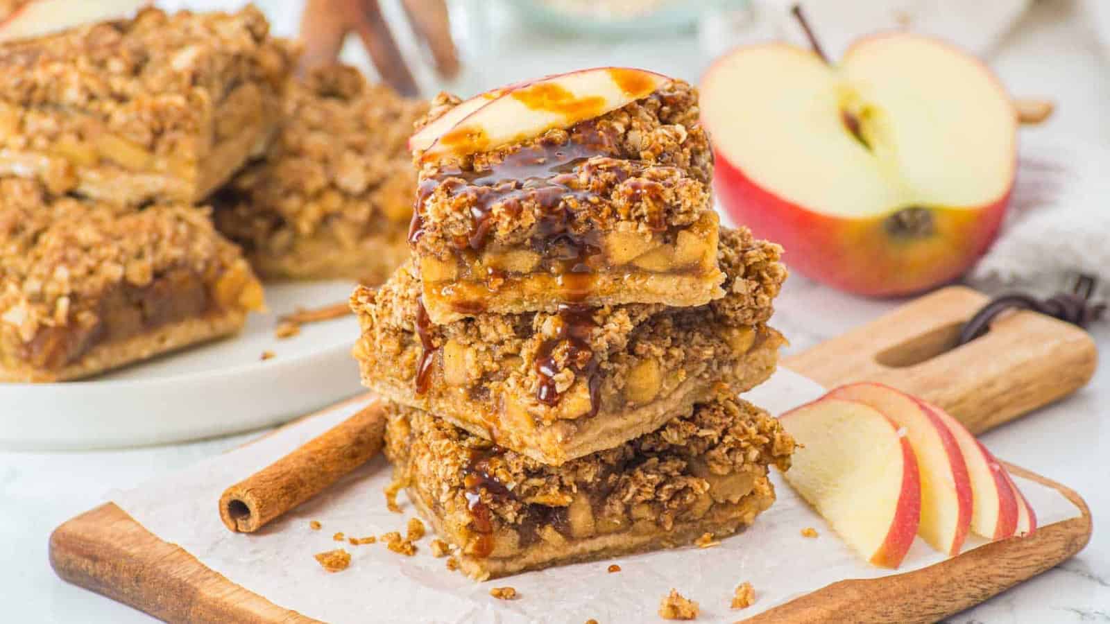 Three stacked apple crumble bars topped with a fresh apple slice, drizzled with caramel sauce.