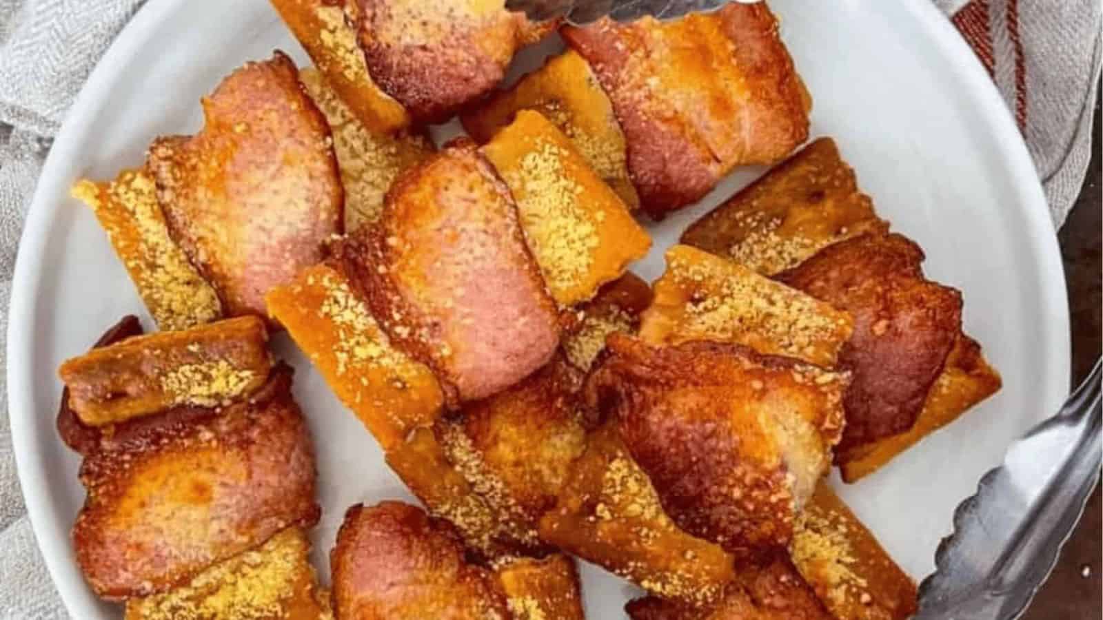 Fingers holding a bacon wrapped crackers.
