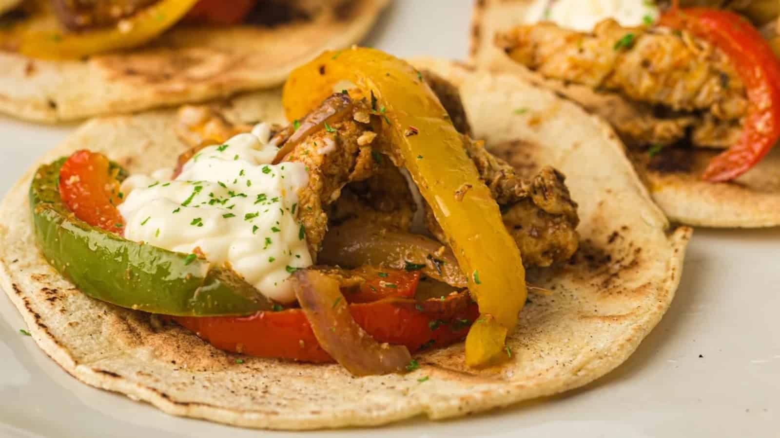 Close-up of a dish featuring seasoned strips of chicken, red and yellow bell peppers, green peppers, and onions.