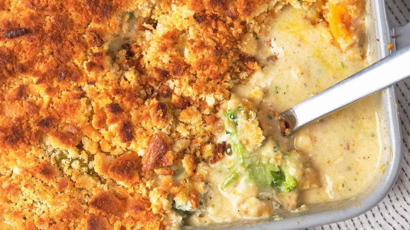 Close-up of a spoon scooping creamy broccoli casserole topped with a golden, crispy layer from a baking dish.