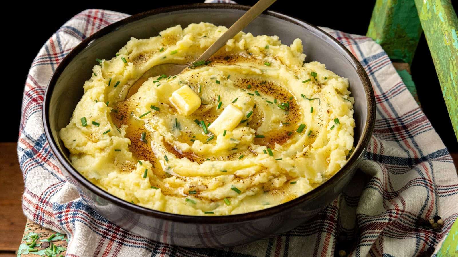 A bowl of mashed potatoes with melted butter, chopped chives, and a spoon.