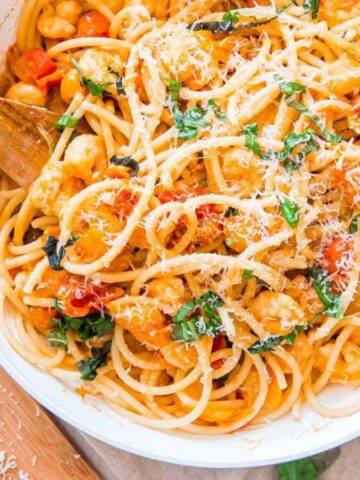 A pan of spaghetti with tomatoes, chickpeas, herbs, and grated cheese, stirred with a wooden spoon.