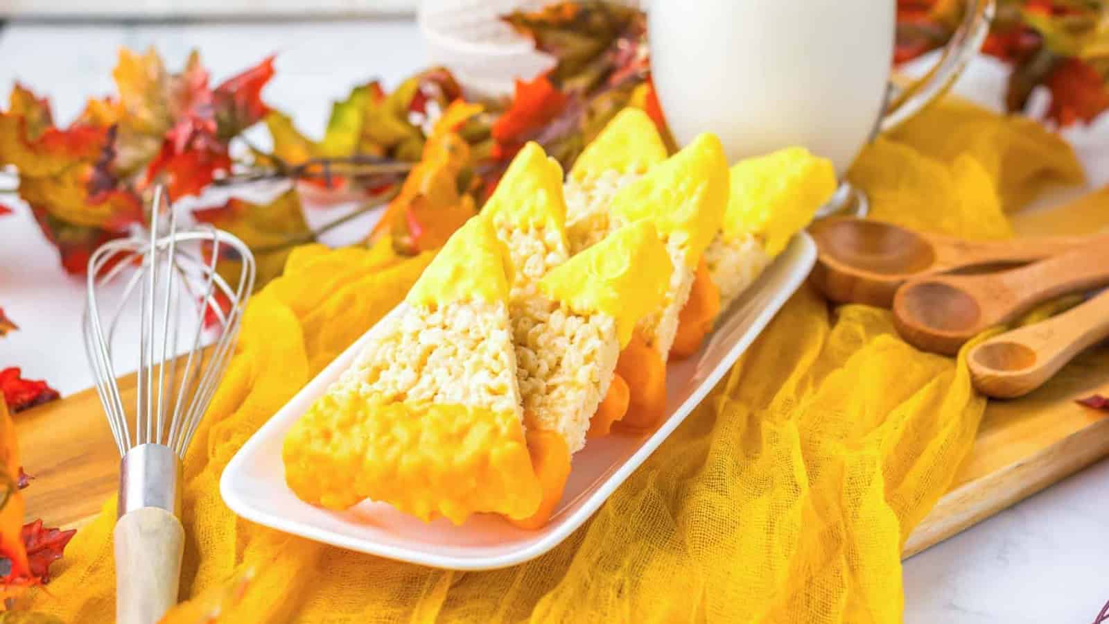 Rice Krispies treats dipped in yellow and orange chocolate, arranged on a white plate with fall decor.