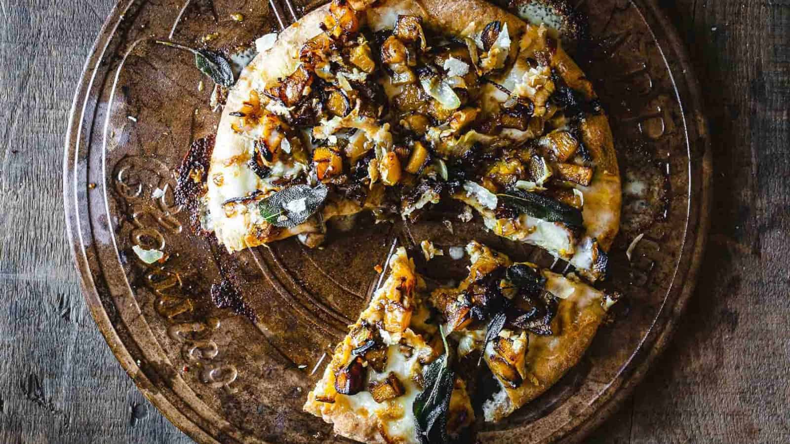 A vegetarian pizza topped with onions and sage, served on a rustic wooden board.