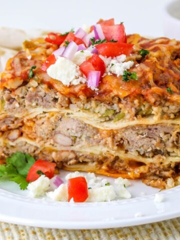 A slice of layered lasagna topped with diced tomato, onion, and cheese on a white plate.