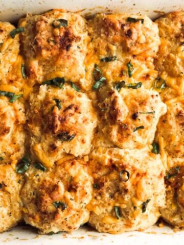 Golden-brown cheesy biscuits baked in a white casserole dish with red handles, garnished with herbs.