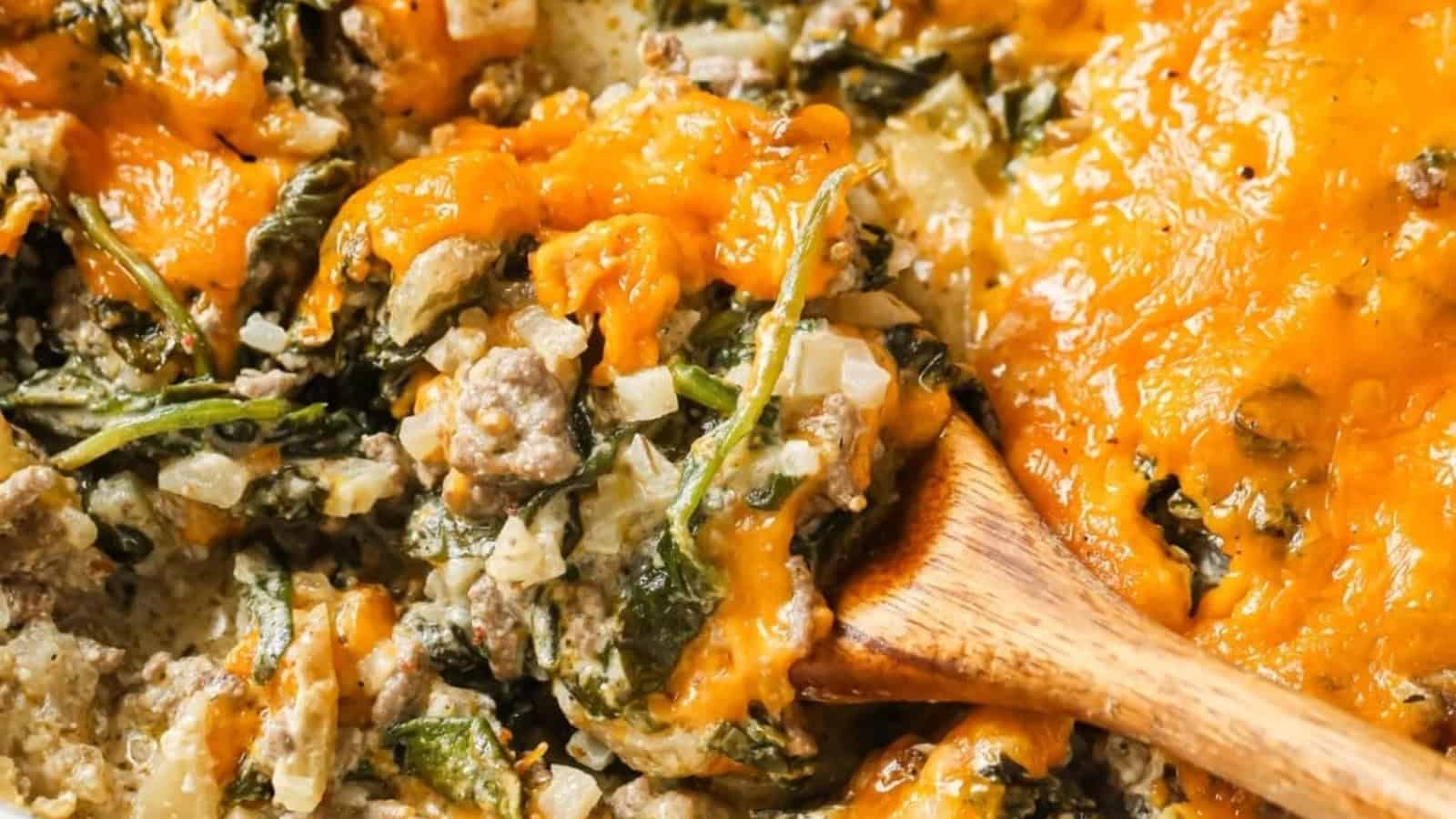 Cheesy beef casserole with cauliflower rice and spinach being spooned out of a baking dish.