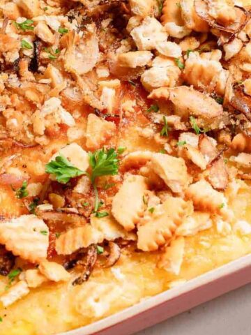 Cheesy casserole topped with crushed crackers and herbs in a red baking dish.