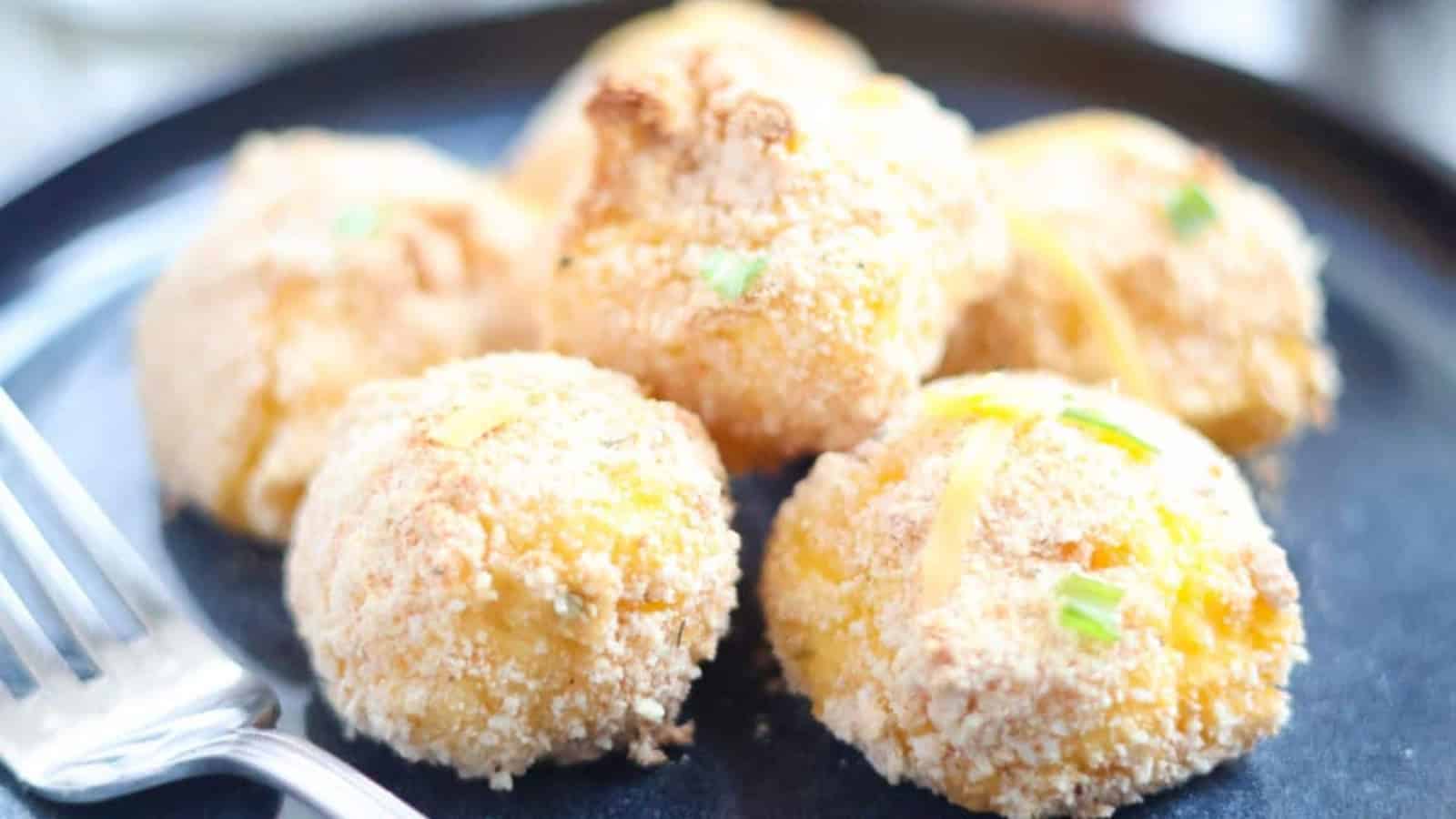 Five cheesy potato puffs on a plate with a fork.