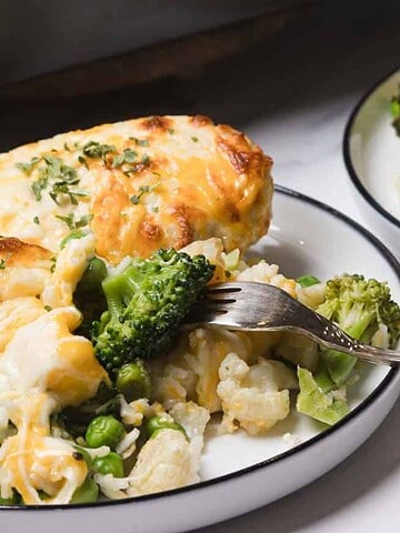 A fork and plate with cheesy baked vegetables including broccoli, peas, and cauliflower.