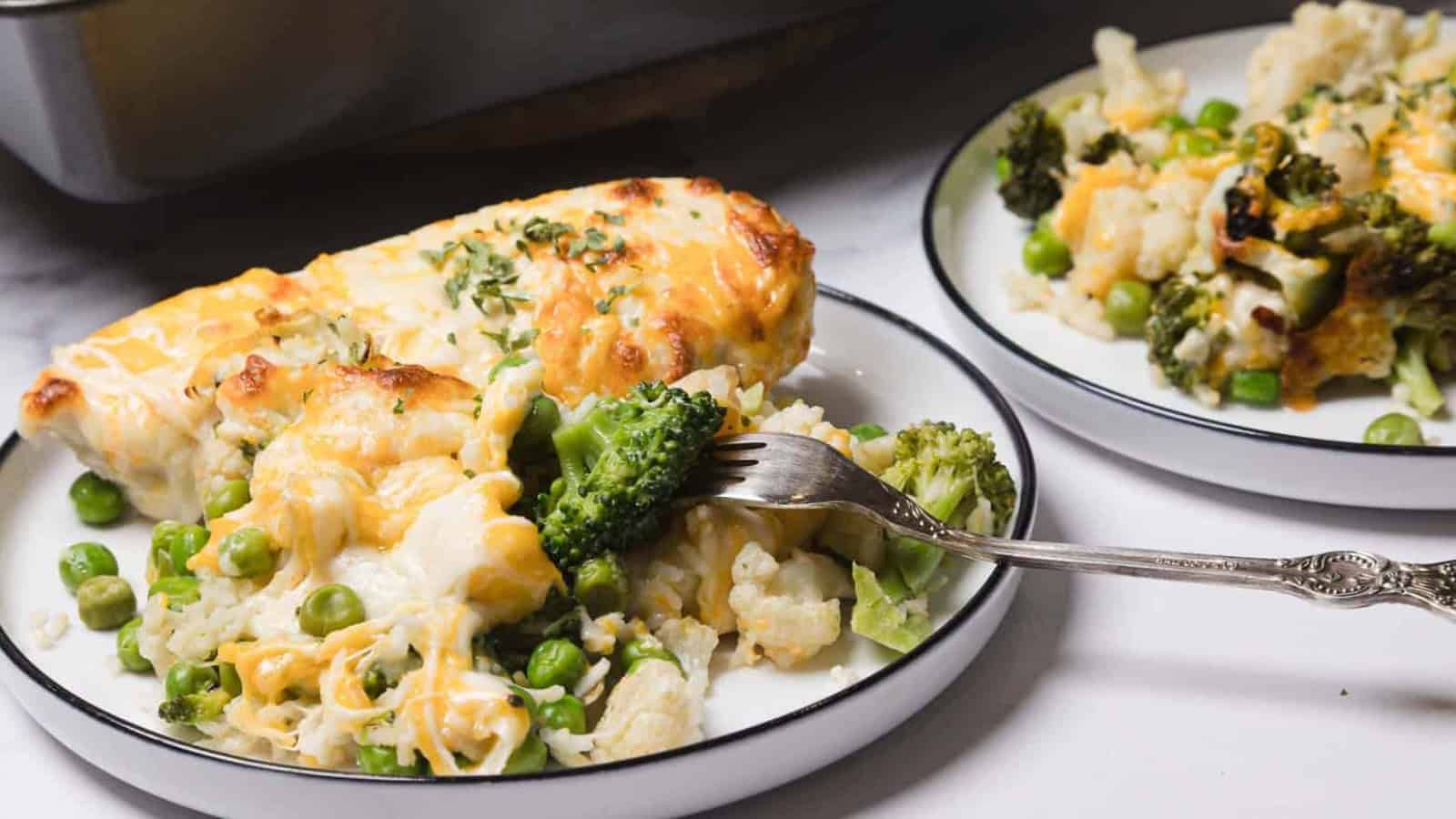 A plate of cheesy vegetable casserole with broccoli, peas, and cauliflower, with a fork lifting a bite.