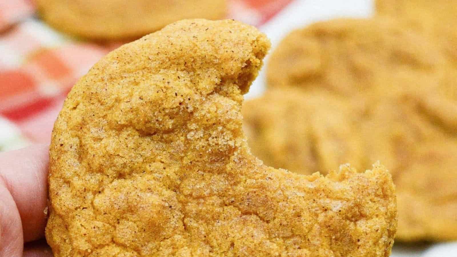 Pumpkin snickerdoodles cookies on a plate with a bite taken out of them.