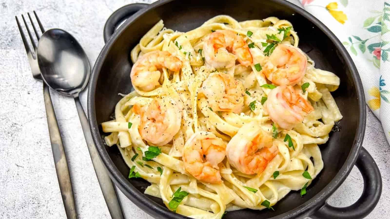 A bowl of olive garden creamy shrimp alfredo pasta served in a black bowl with a spoon.