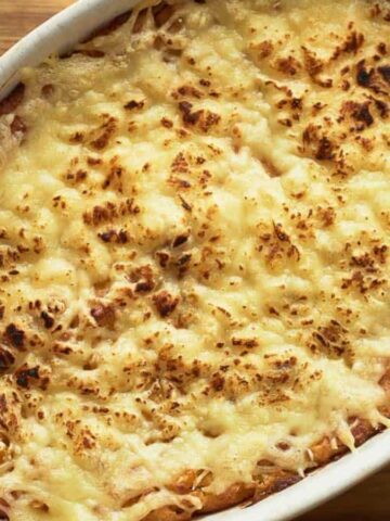 Baked casserole topped with golden, melted cheese in a white oval dish on a wooden surface.