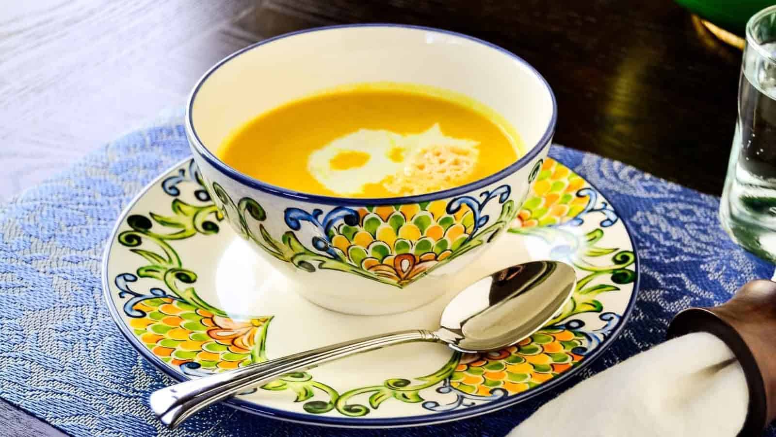 A bowl of butternut squash soup with a spoon on a colorful blue and white plate.