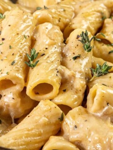 Creamy rigatoni pasta topped with black pepper and fresh thyme, served with a fork.