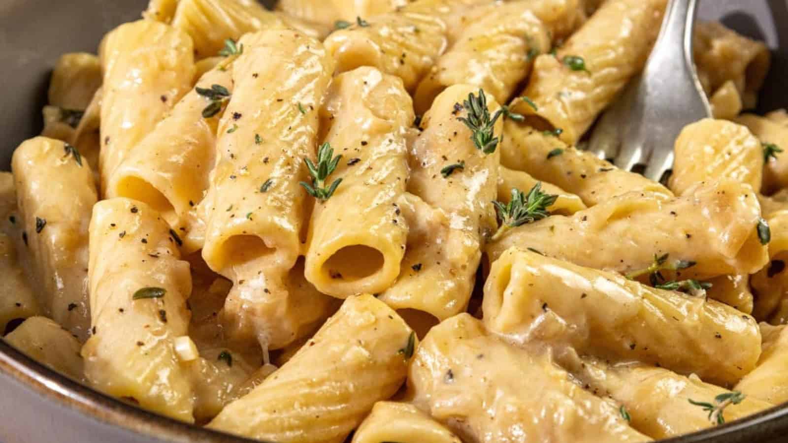 A close-up of creamy French onion pasta rigatoni with caramelized onions, garnished with fresh thyme and cracked black pepper, served in a bowl with a fork.