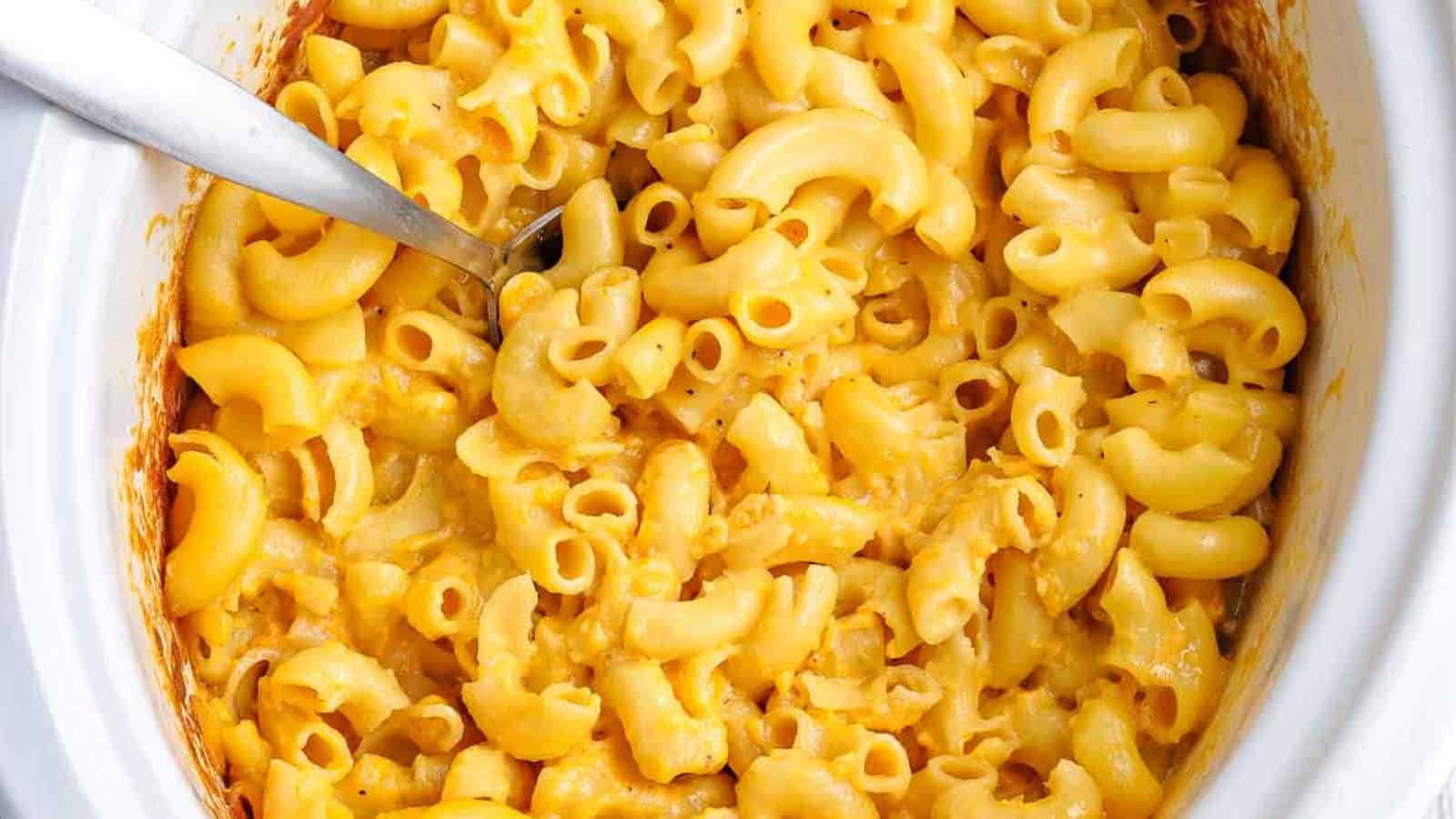 A bowl of macaroni and cheese in front of a slow cooker.