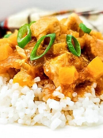 A plate of white rice topped with curry and sliced green onions, with a napkin in the background.