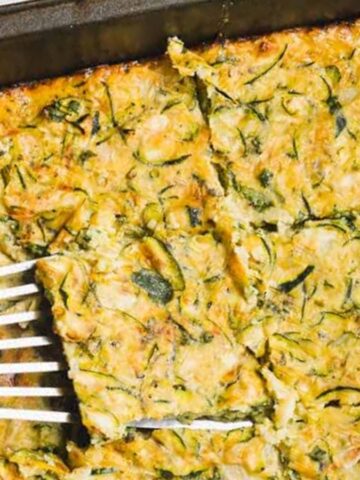 A spatula lifts a square piece of baked zucchini casserole from a baking pan.