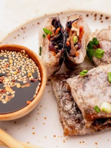 Plate with crispy spring rolls cut open, served with soy dipping sauce and chopsticks on the side.