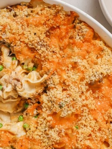 Baked casserole with noodles, peas, and a crispy breadcrumb topping, served in a white dish with a portion in a bowl.