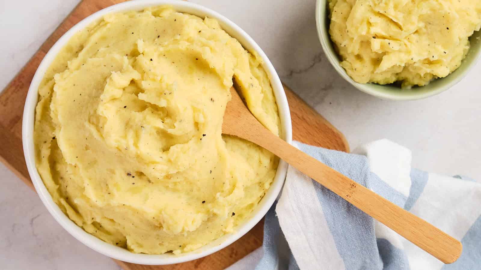A bowl of garlic mashed potatoes with a wooden spoon resting on top.