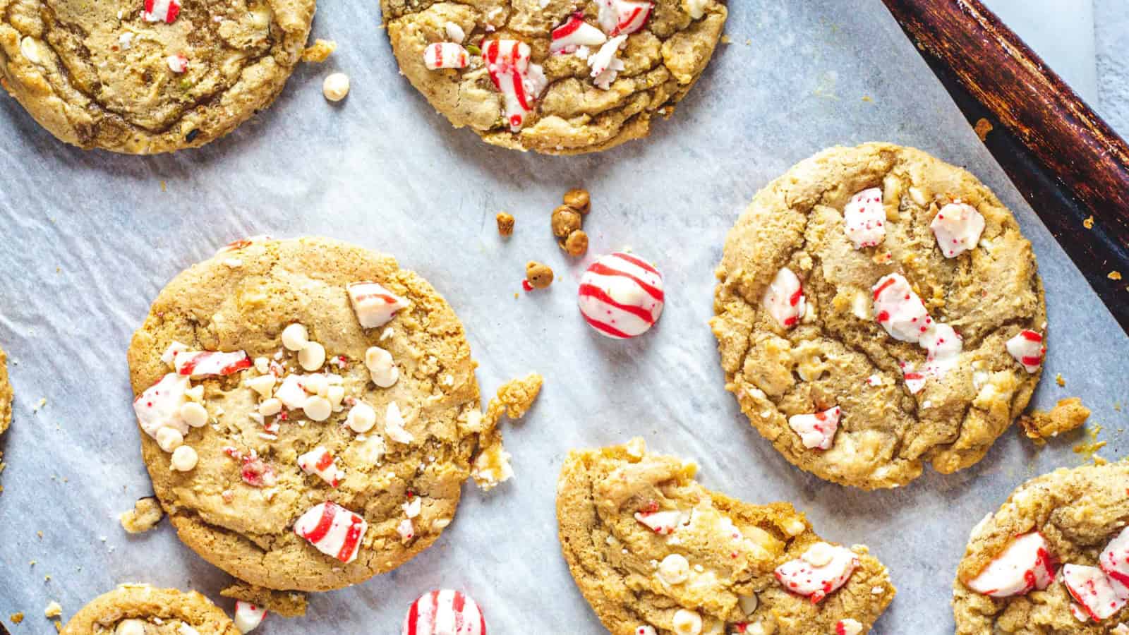 Cookies with white chocolate chips and crushed peppermint candies on parchment paper.