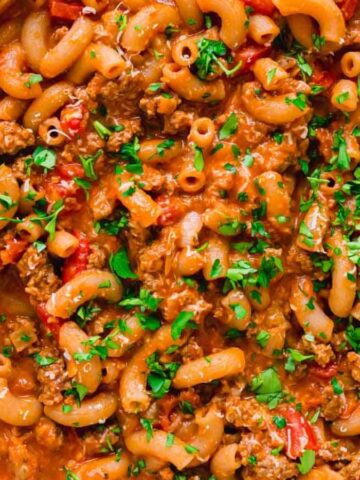 A skillet of creamy beef and macaroni pasta topped with chopped parsley on a striped cloth.