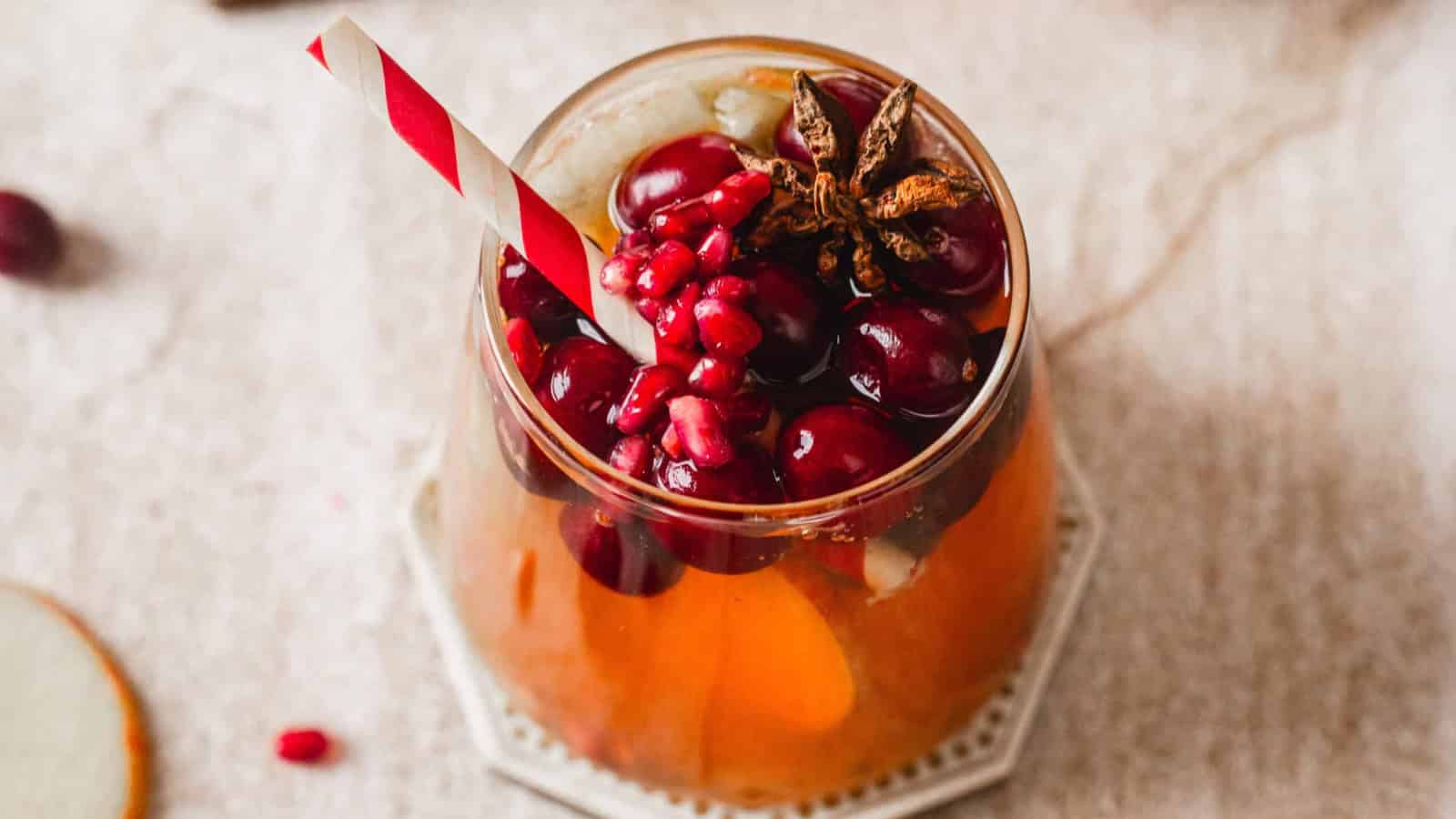 A festive drink garnished with cranberries, pomegranate seeds, ice, and a striped straw in a glass.