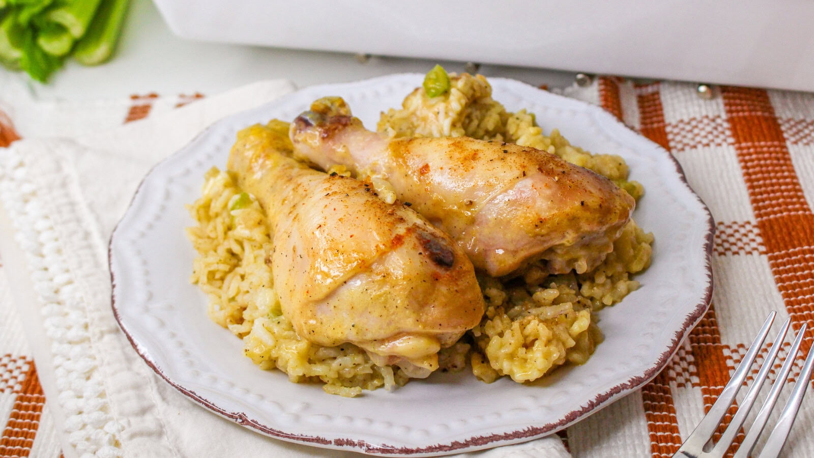Plate with chicken drumsticks on a bed of seasoned rice, placed on a checkered tablecloth with a white napkin and a fork nearby.