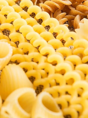Assorted uncooked pasta shapes, including shells, spirals, and rotini, arranged closely together.