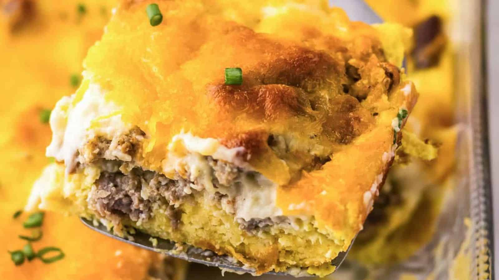 A slice of baked breakfast casserole with melted cheese on top being lifted from a dish.