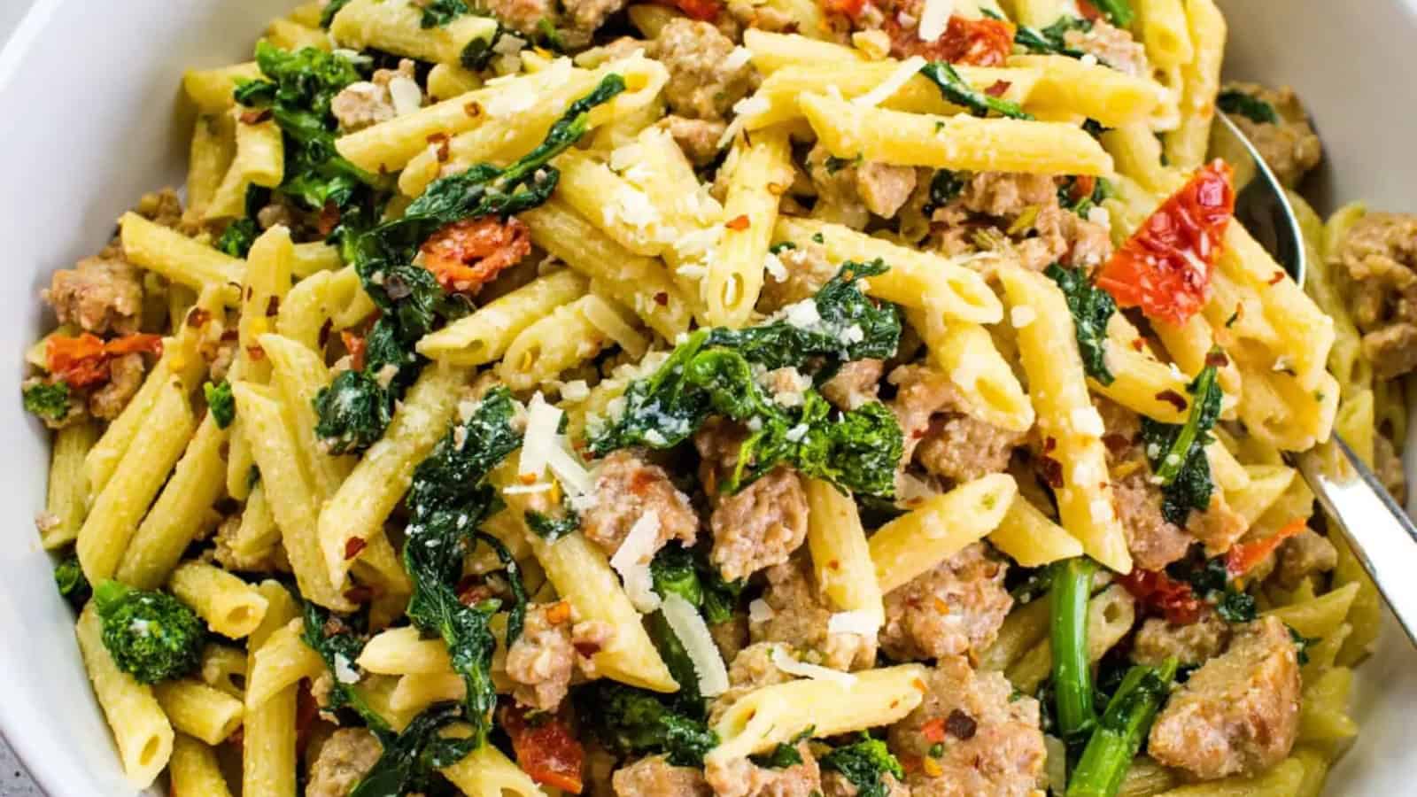 Broccoli Rabe and Sausage in a serving bowl with tomatoes in the background.